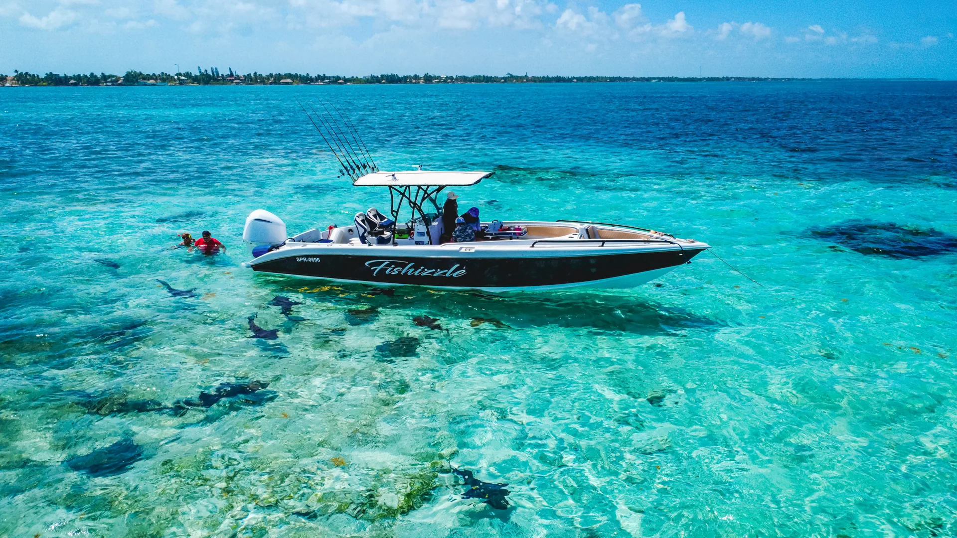 Fishizzle anchored in turquoise water, with swimmers beside the boat